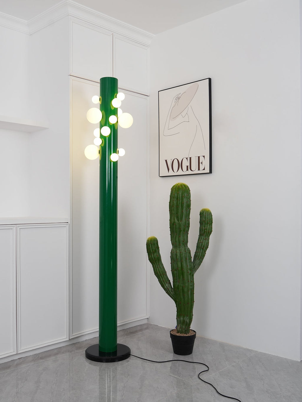 A potted cactus now stands beside the green Clérachic floor lamp, its globes glowing warmly in the same white corner.