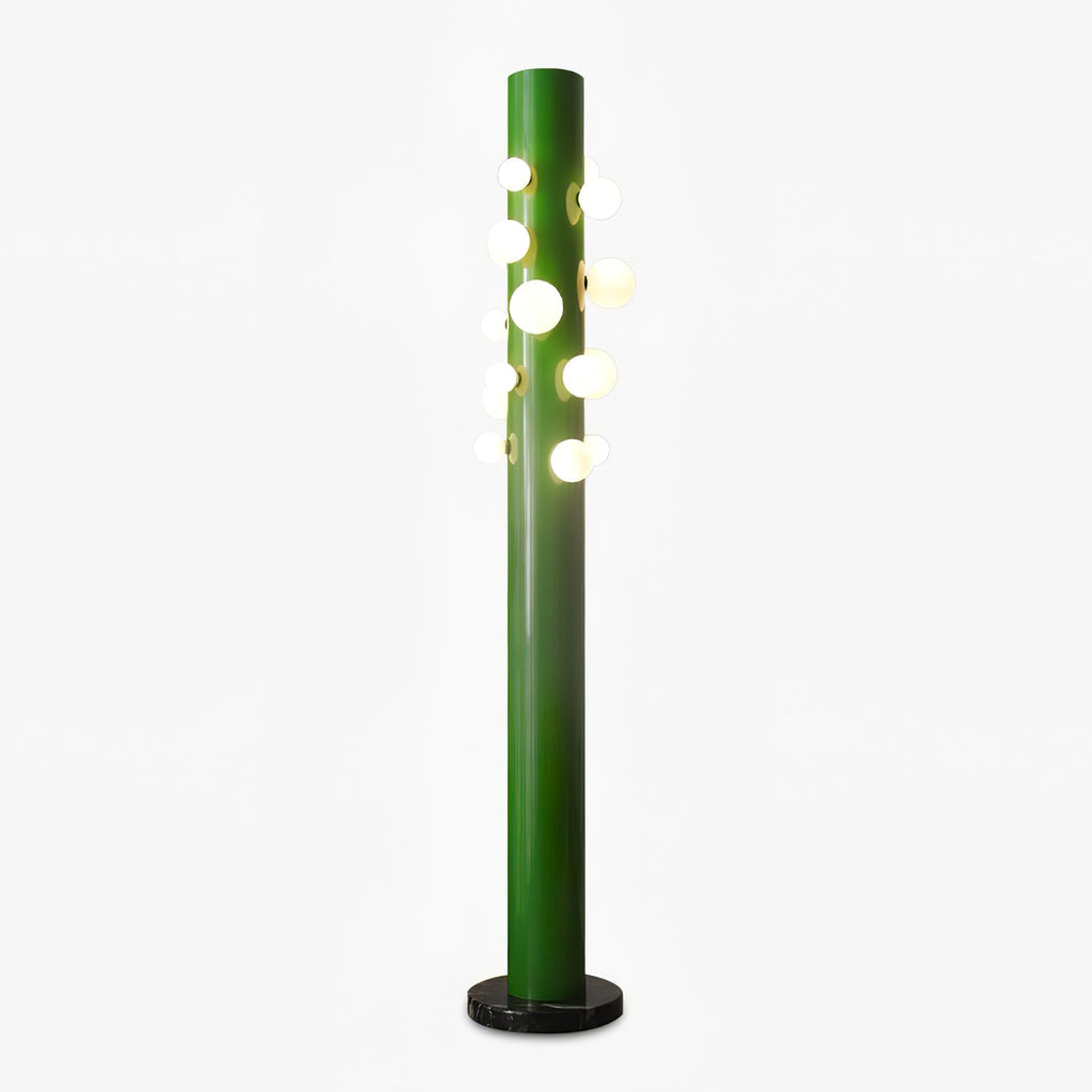 A green metal Clérachic floor lamp stands alone on white, its cluster of frosted glass globes glowing beside a round black marble base.