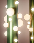 An abstract close-up catches the green Clérachic floor lamp's glass globes reflected against a soft rose-toned backdrop.