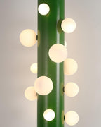 Another macro crop shows the green Clérachic floor lamp's frosted globes glowing warmly against its plain painted backdrop.