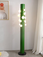 Beside a sheer curtain and a framed abstract print, the green Clérachic floor lamp lights a corner of pale wood flooring.