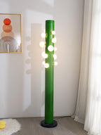 A sheepskin rug sits at the foot of the green Clérachic floor lamp, positioned beneath a framed abstract print on the wall.