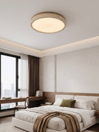 This round Clérachic ceiling light glows above a bed with an olive cushion, facing a floor-to-ceiling window and city view.