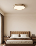 This round Clérachic ceiling light glows above a bed with a tufted headboard and camel-toned bedding.