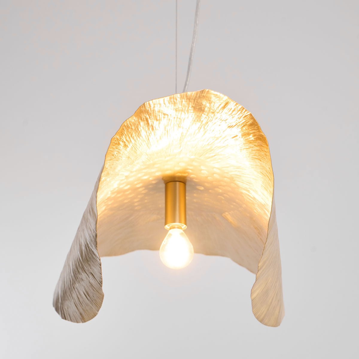 Seen from below, this Clérachic shade's lit bulb sits inside its flower-like brass folds.