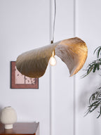 Lit gold, this Clérachic hammered brass shade hangs near a side table with a white sculpture.
