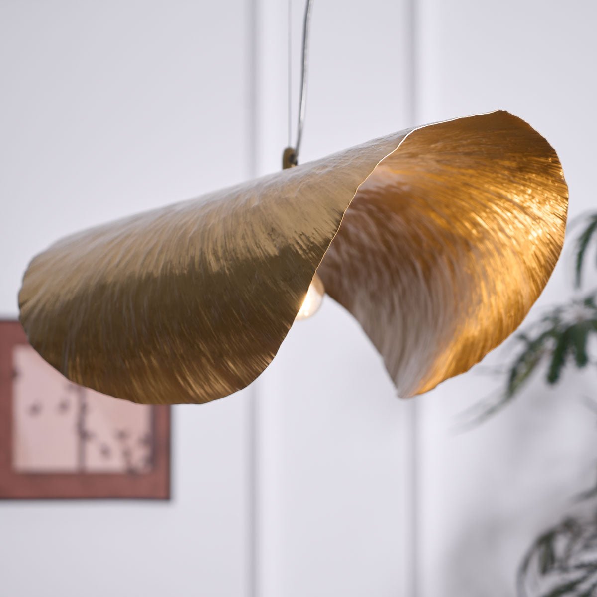 A closer view shows this Clérachic shade lit gold beside the same framed print and plant.
