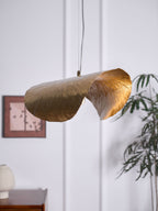 Unlit, this Clérachic hammered brass shade hangs beside a framed print and a potted plant.