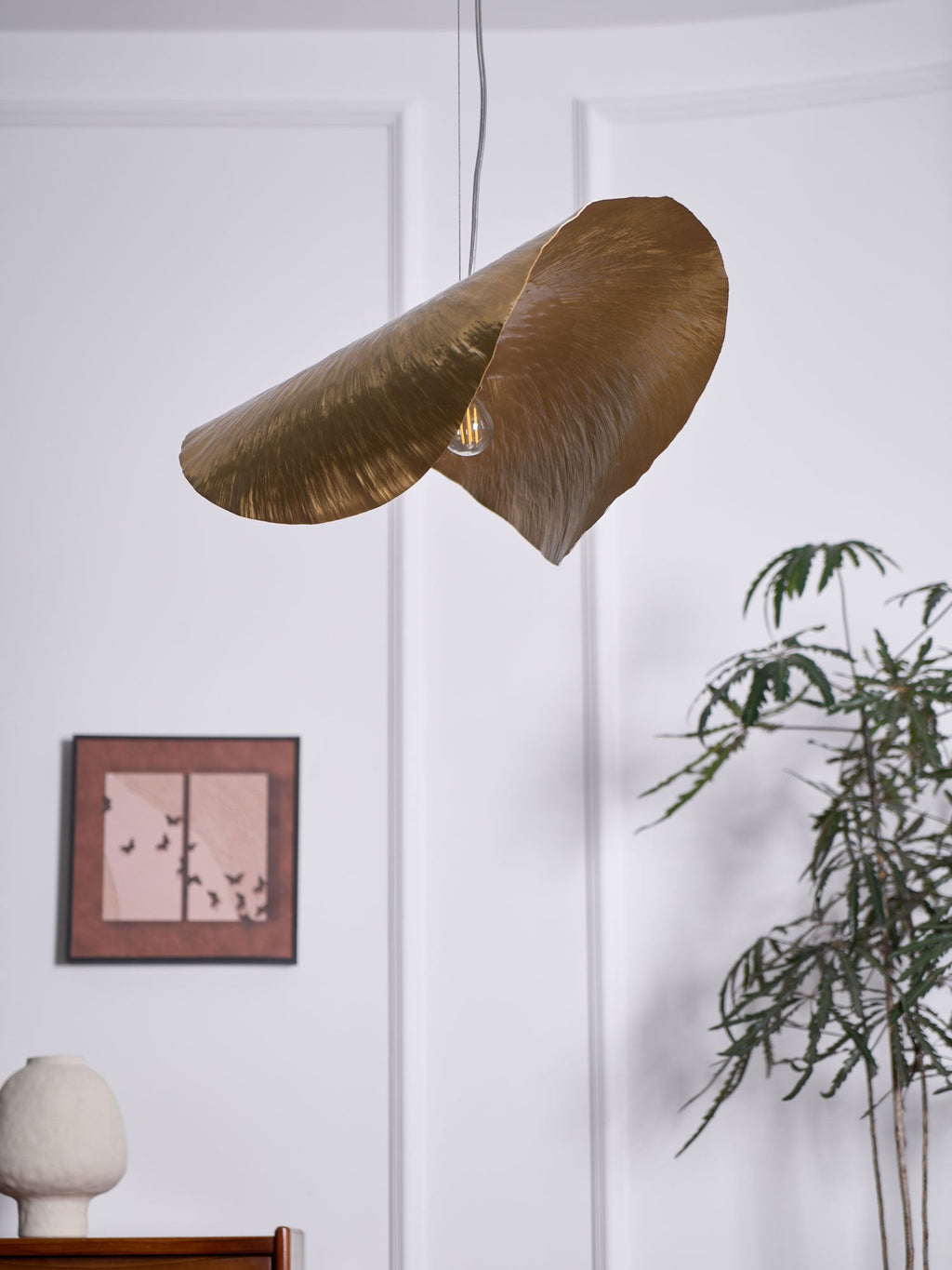This Clérachic hammered brass shade hangs unlit again beside the framed print and potted plant.