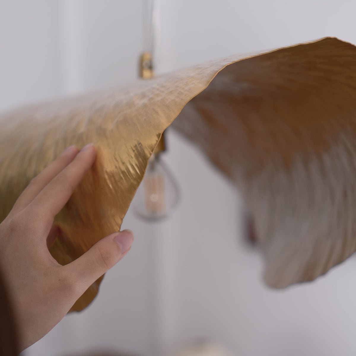 A hand touches the textured edge of this Clérachic hammered brass shade in close-up.