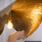 A hand lifts the edge of this Clérachic shade, its filament bulb glowing warm inside.