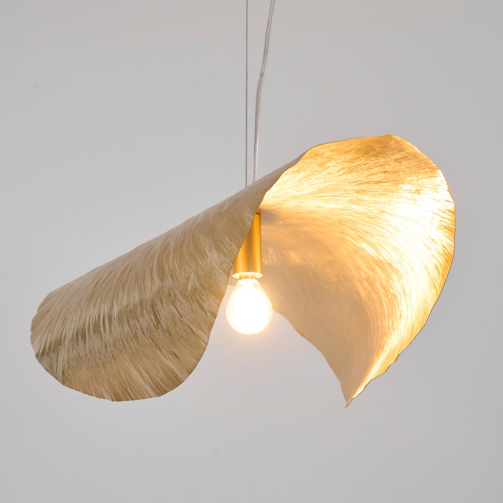 The bulb glows between the folded brass lobes of this Clérachic pendant, shown at an angle.