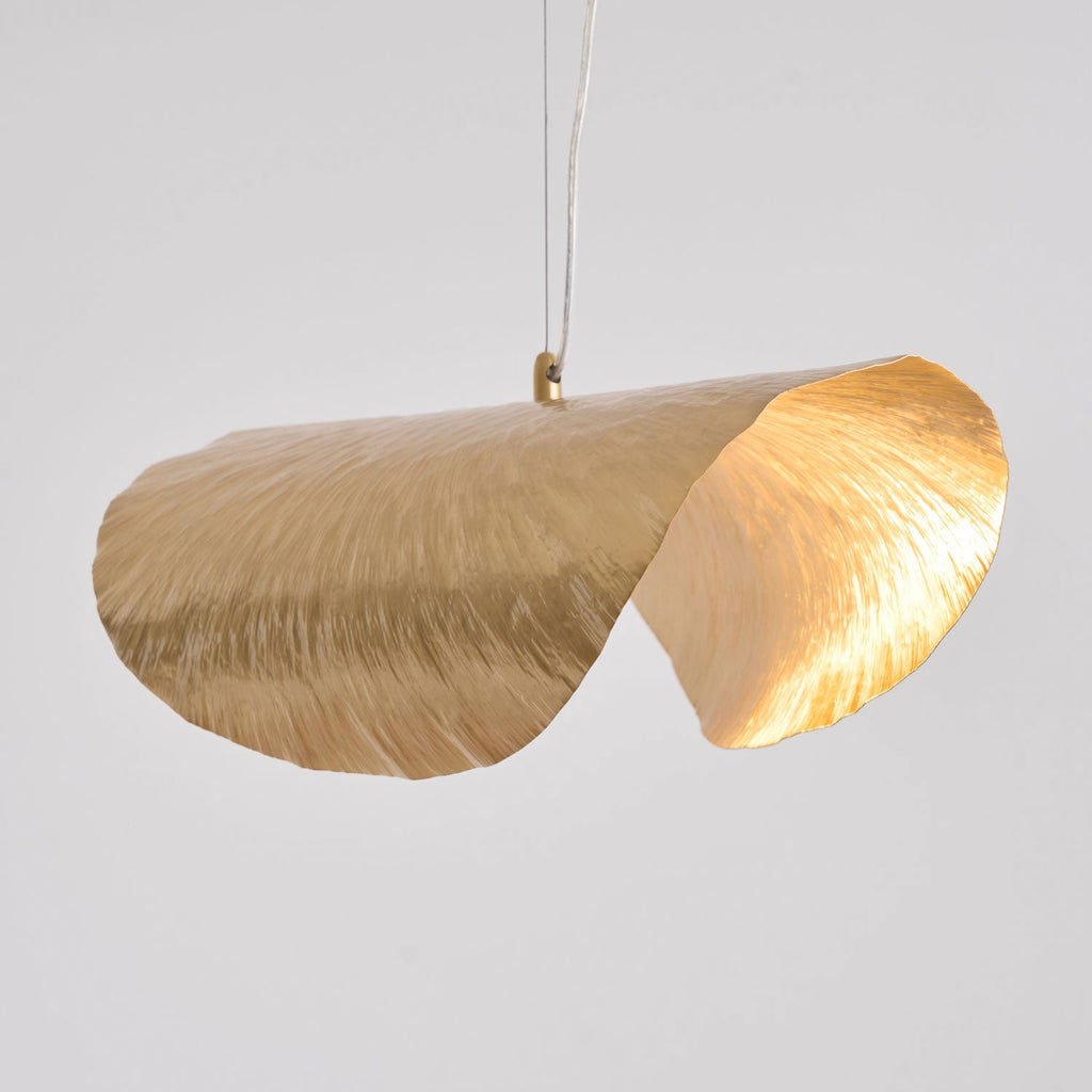 Seen from the side, this Clérachic hammered brass shade curls into two lit lobes on grey.