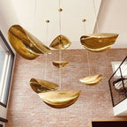 A cluster of hammered brass shades from Clérachic hangs at staggered heights against an exposed brick wall.