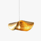 Two hammered brass shades curve together, lit gold, in this Clérachic pendant's studio close-up.
