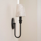 This Clérachic sconce in black hardware shows its U-loop arm from the side, alabaster shade against a plain wall.