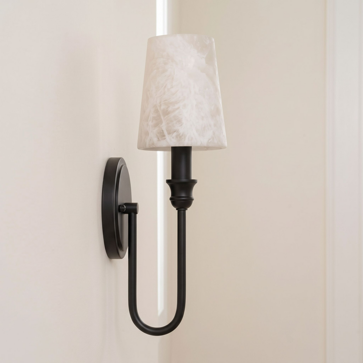 This Clérachic sconce in black hardware shows its U-loop arm from the side, alabaster shade against a plain wall.