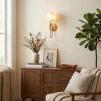 Near a sideboard with a plant and framed art, this Clérachic sconce in brass hardware glows warm on the wall.
