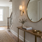 Beside a round mirror above a console table in a hallway, this Clérachic sconce in brass hardware glows warm.