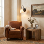 This matte black Clérachic wall sconce arcs its gooseneck arm over an alabaster cone shade, glowing beside a leather armchair.
