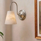 Unlit, this brushed nickel Clérachic wall sconce shows its gooseneck arm and alabaster cone shade beside a framed painting.