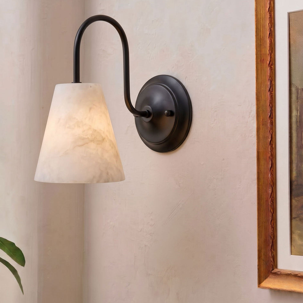 This matte black Clérachic wall sconce hangs unlit, its alabaster cone shade catching light beside a framed painting edge.
