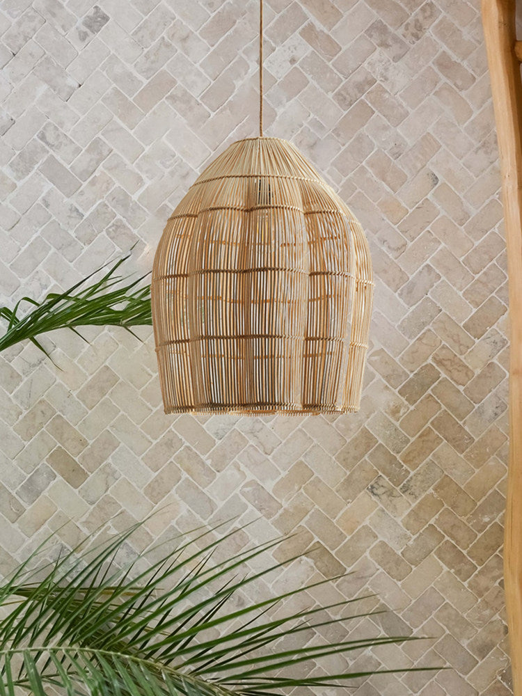 Against a herringbone stone wall, this Clérachic pendant's woven rattan dome hangs beside a palm leaf.