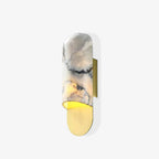 Clérachic marble cylinder wall light with a warm glow at its brass base plate, shown alone on a white background.