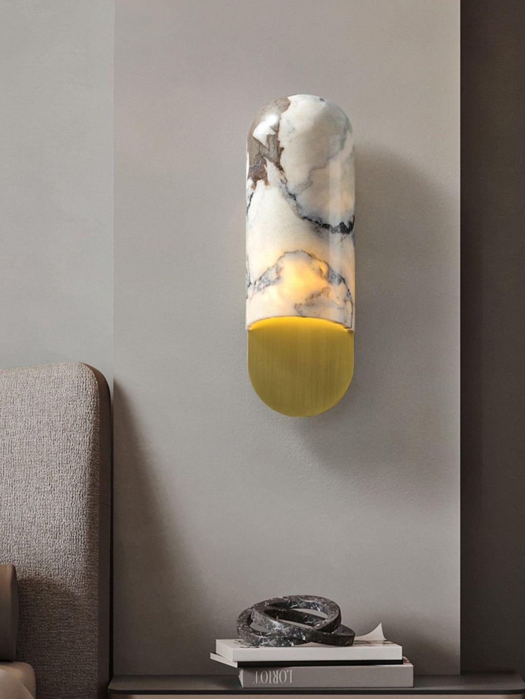 Above a console shelf holding a stack of books and a small ornament, the Clérachic marble cylinder wall light glows warm.