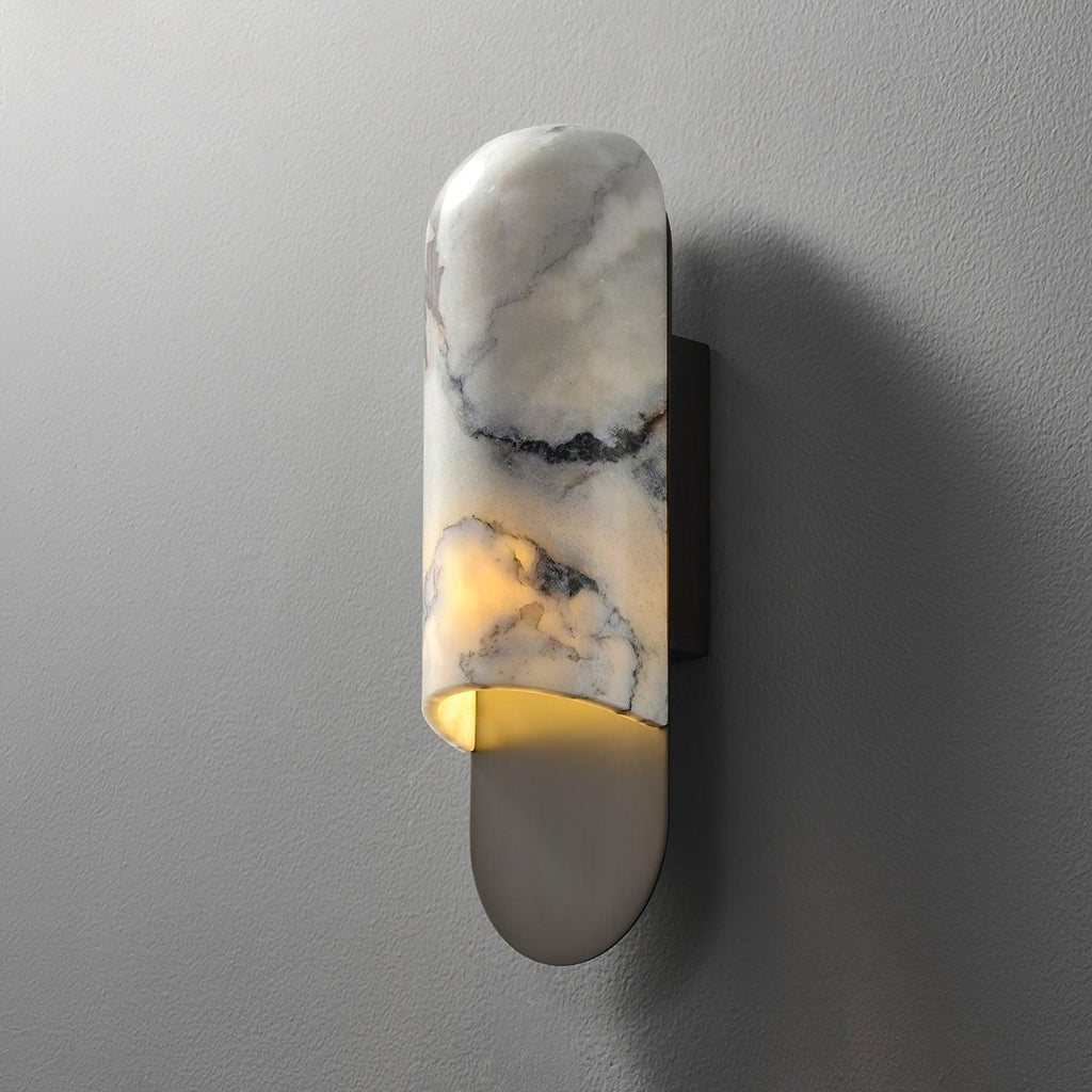 Clérachic marble cylinder wall light unlit on a textured grey wall, its curved backplate cast with a soft side shadow.