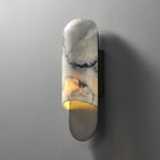 Clérachic marble cylinder wall light unlit on a textured grey wall, its curved backplate cast with a soft side shadow.