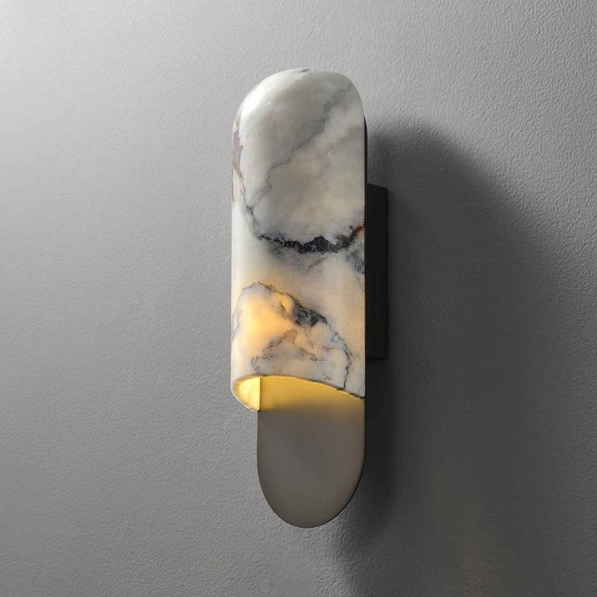 Clérachic marble cylinder wall light unlit on a textured grey wall, its curved backplate cast with a soft side shadow.