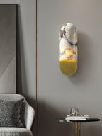 Warm light spills from the Clérachic marble cylinder wall light beside a mirrored panel, above a grey armchair and round side table.