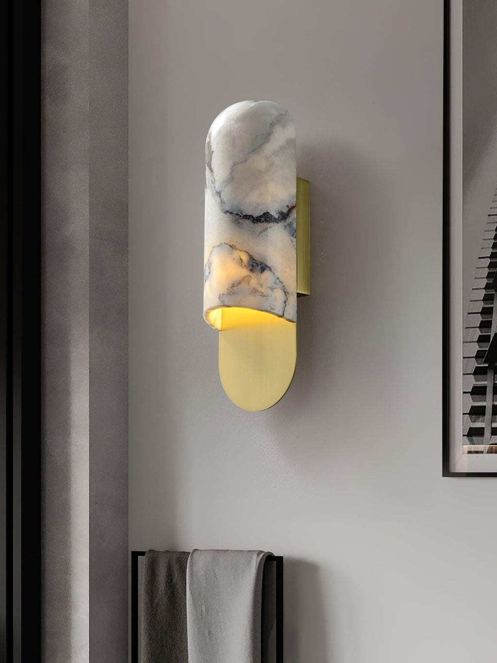 Beside a framed print, the Clérachic marble cylinder wall light glows warm, a folded towel hung on the rail below it.
