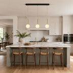 Three Clérachic sphere pendants line a black bar above a kitchen island with grey stools.