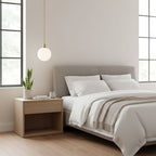 A single brass-and-white Clérachic sphere pendant hangs lit beside a bed with a grey headboard.