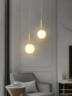 A panelled wall and armchair sit beneath two brass-and-white Clérachic sphere pendants at staggered heights.