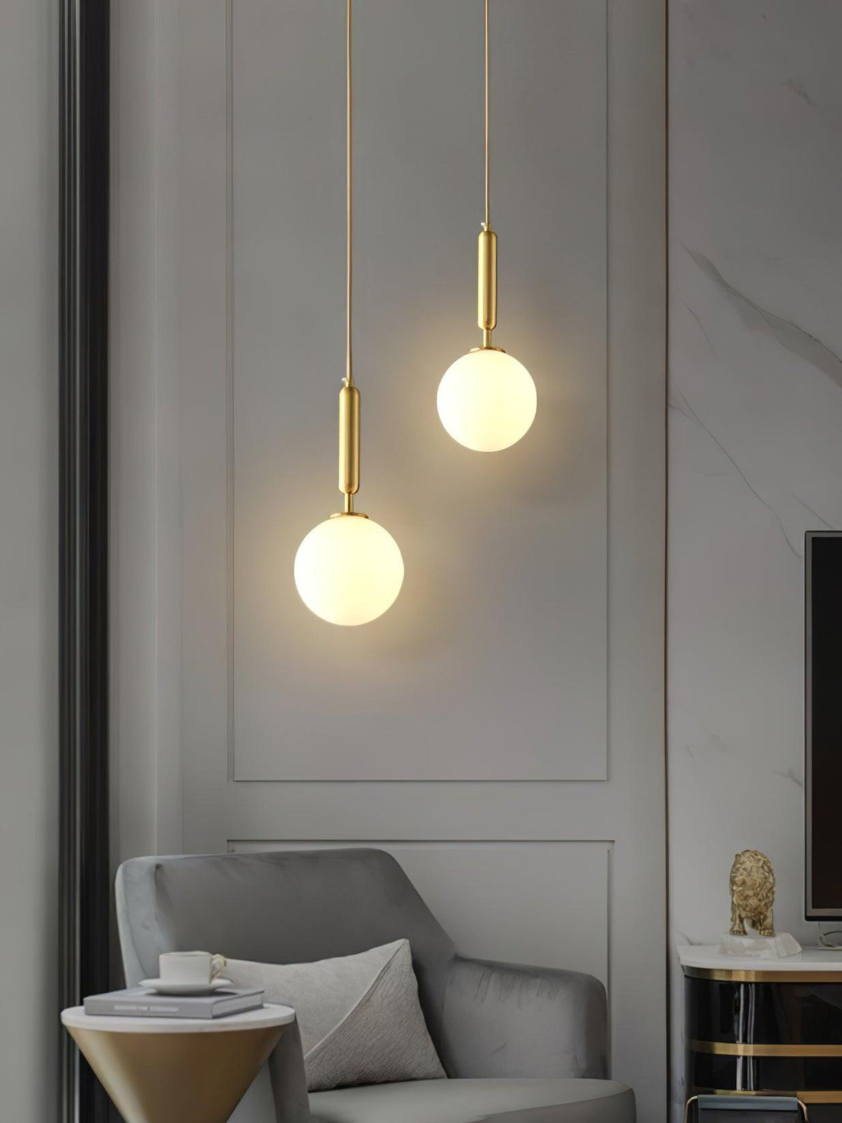 A panelled wall and armchair sit beneath two brass-and-white Clérachic sphere pendants at staggered heights.