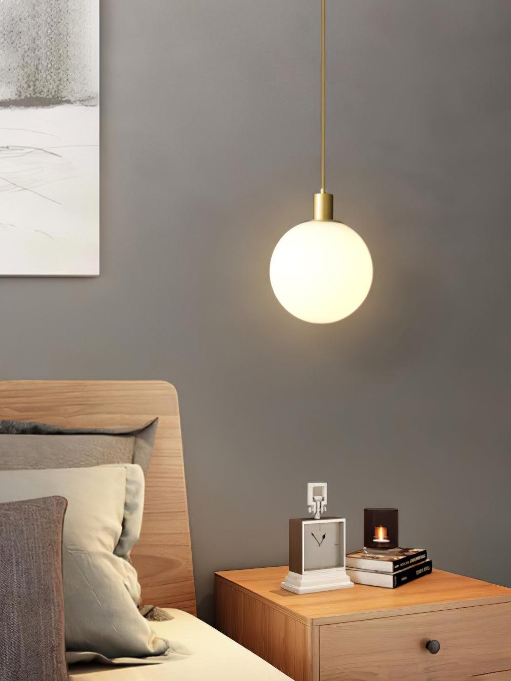 A single brass-and-white Clérachic sphere pendant lights a nightstand with a clock and candle.