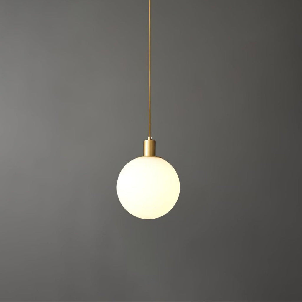 A single Clérachic sphere pendant hangs from a thin brass cord against a dark grey backdrop.