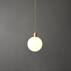 A single Clérachic sphere pendant hangs from a thin brass cord against a dark grey backdrop.