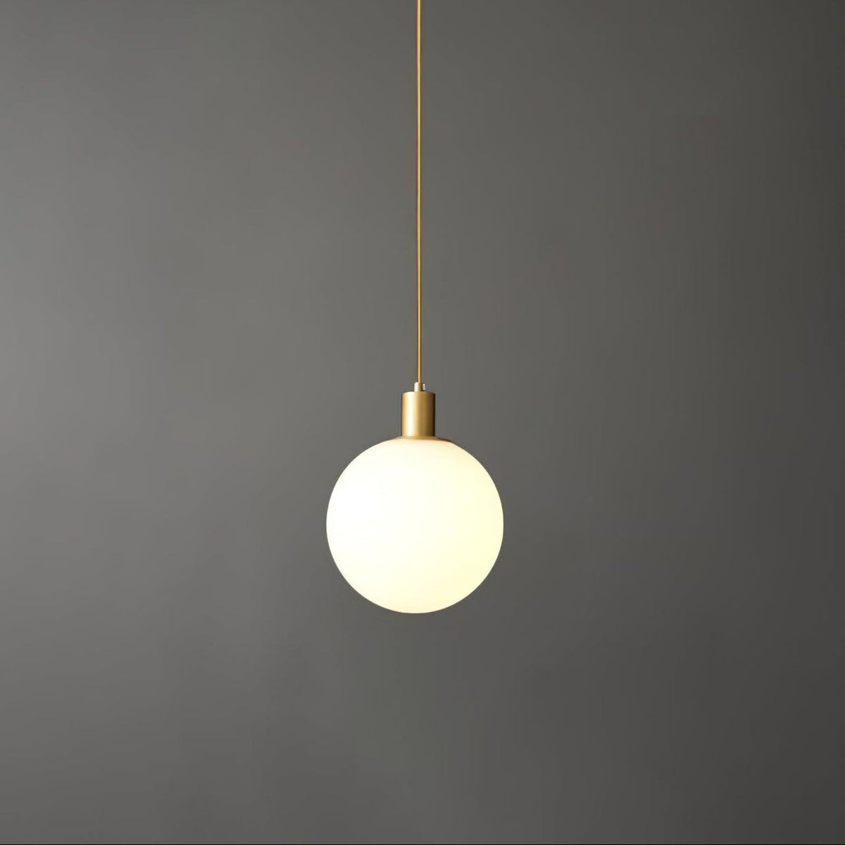 A single Clérachic sphere pendant hangs from a thin brass cord against a dark grey backdrop.