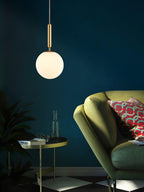 A single brass-and-white Clérachic sphere pendant hangs against a dark teal wall beside a green chair.