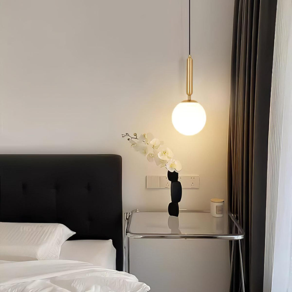 A single Clérachic sphere pendant in brass and white lights a bedside table with an orchid.