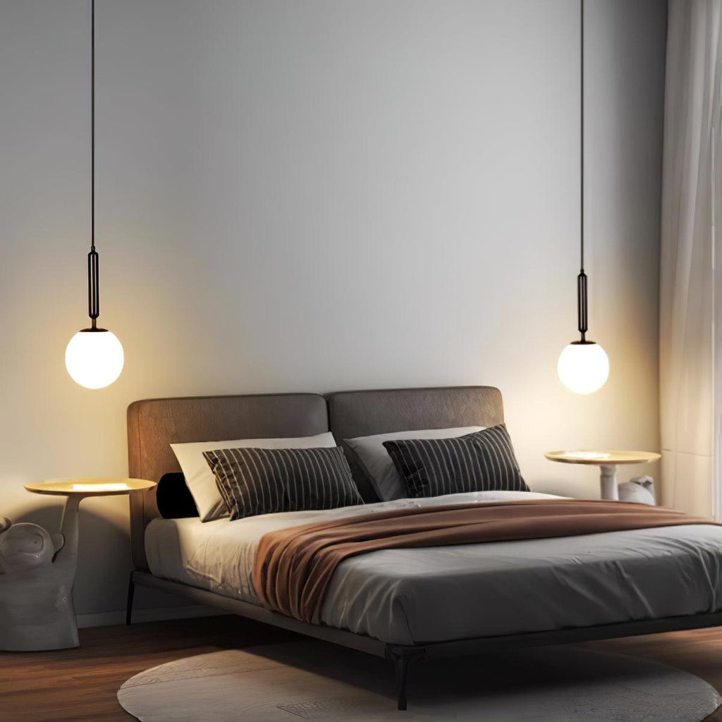 Two single-drop Clérachic sphere pendants in black and white flank a bed in a grey room.