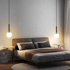 Two single-drop Clérachic sphere pendants in black and white flank a bed in a grey room.