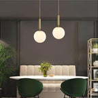 Two brass-and-white Clérachic sphere pendants hang above a banquette dining nook with green chairs.