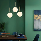 A green wall backs three brass-and-white Clérachic sphere pendants above this dining table.