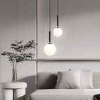 Near a sofa and potted plant, two black-and-white Clérachic sphere pendants hang at different heights.