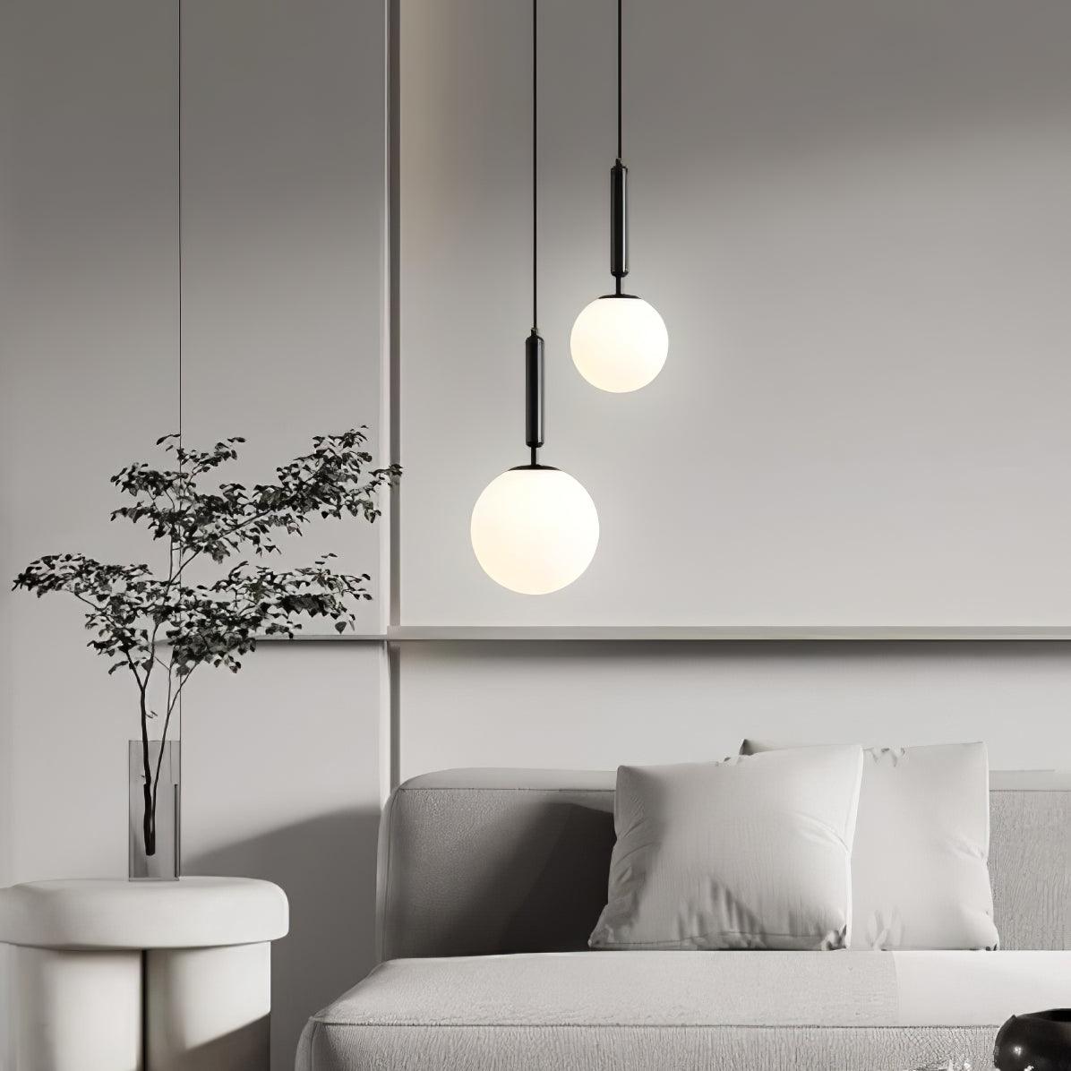 Near a sofa and potted plant, two black-and-white Clérachic sphere pendants hang at different heights.